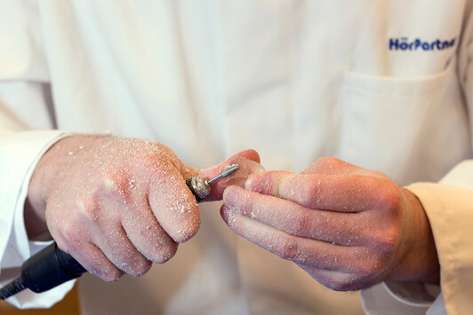 Ein Hörakustiker bearbeitet ein Hörgerät handwerklich mit einem Schleifwerkzeug.